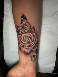 a black and white rose tattoo with a butterfly on it's arm, sitting on a person's leg