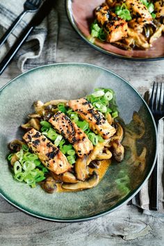 two plates with chicken, mushrooms and green onions on them next to a fork and knife