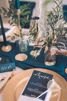 the table is set with gold and blue place settings, silverware, and greenery