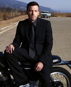 a man in a suit and tie sitting on a motorbike by the road