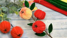 three orange flowers sitting next to each other on top of a wooden table with green leaves