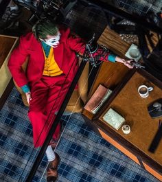 a man in a red suit and clown makeup is standing next to a table with other items on it