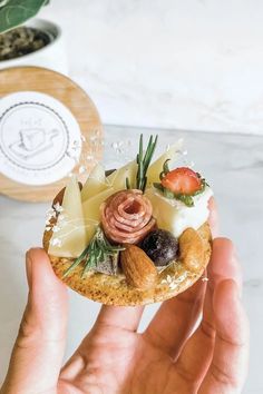 a person is holding up a pastry with fruit and nuts on it in front of a potted plant