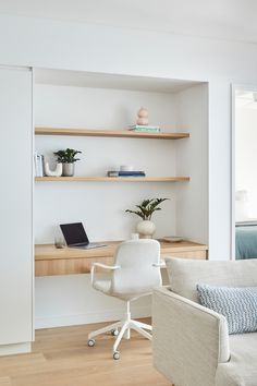 Inner-city apartment renovation showing a study nook built next to custom white joinery. The study nook features a pale timber floating desk with drawers & open timber shelving above. The shelves are styled with books, plants & ceramic items. A white office chair also sits at the desk behind an open laptop. The edge of a pale grey sofa with a blue patterned cushion and blue-grey throw can be seen in the foreground. The master bedroom, in similar tones of blue, can be seen just out of frame. Built In Office Nook In Living Room, Open Plan Study Area, Desk Alcove Built Ins, Study In Lounge Room, Hamptons Study Nook, Study Nook Cabinetry, Study Nook In Kitchen, Built In Workspace, Study Nook In Bedroom