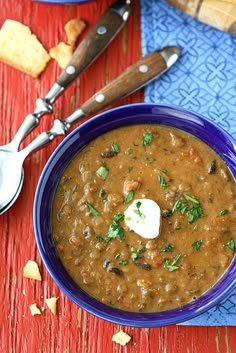 a blue bowl filled with soup next to two spoons on top of a red table