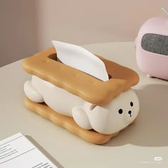 a white and brown bear shaped tissue dispenser next to a pink alarm clock