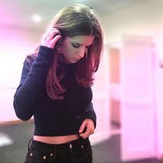 a woman with long hair is looking at her cell phone while standing in a room