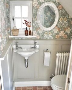 the bathroom is decorated with floral wallpaper and has a white sink, toilet, and window