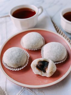 three pastries on a pink plate next to two cups of tea