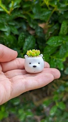 a hand holding a tiny white bear with succulents in it's mouth