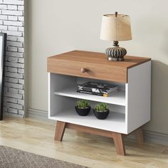 a nightstand with two plants on it next to a brick wall and a lamp in the corner