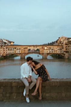 a man and woman sitting on the edge of a bridge