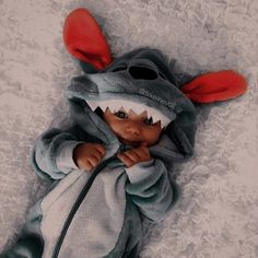 a baby doll is dressed in a shark costume with red ears and tail, while laying on the floor