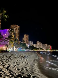 the beach is lit up at night with palm trees and buildings in the back ground