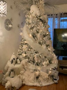 a white christmas tree decorated with silver ornaments and snowflakes, surrounded by stuffed animals