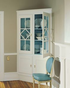 a blue chair sitting in front of a white china cabinet with glass doors on it