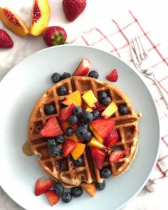 a white plate topped with waffles covered in fruit next to sliced peaches and blueberries