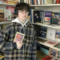 a young man wearing headphones and holding a book in front of bookshelves