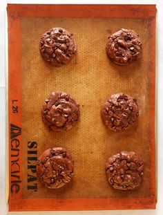 six chocolate cookies sitting on top of a cookie sheet in an orange tray with words above it