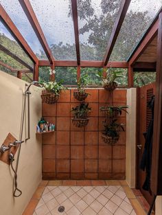 a bathroom with tiled floor and walls has plants on the wall, potted planters hanging from the ceiling