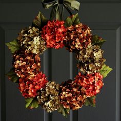 a wreath with red and green flowers hanging from the front door, next to a black door