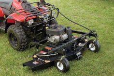 a red lawn mower sitting on top of a green grass covered field next to a black tractor