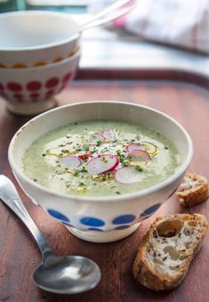 a bowl of soup with radishes and bread on a table next to a spoon