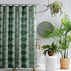 a green shower curtain next to two potted plants and a mirror on the wall