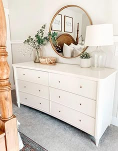 a white dresser topped with lots of drawers and a round mirror on top of it