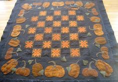 a quilted table runner with pumpkins and leaves on it, sitting on a wooden floor