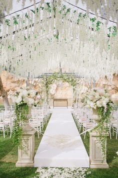 an outdoor ceremony with white flowers and greenery on the aisle, surrounded by chairs