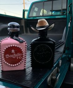 two bottles are sitting on the back of a pickup truck, one with a cowboy hat