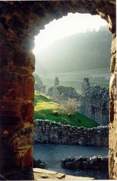 an arch in the side of a stone building with grass and mountains in the background