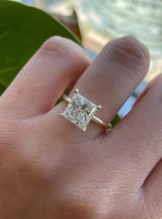 a woman's hand with a diamond ring on top of her finger, next to a green leaf