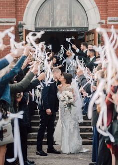 a bride and groom kissing in front of their wedding party with confetti streamers