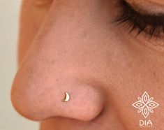 a woman's nose has a small gold crescent piercing on it, with the word dia written in white