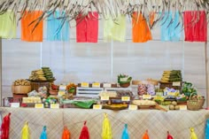 a table topped with lots of food and colorful tassels hanging from the ceiling