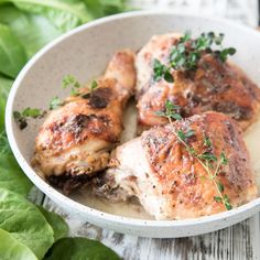 three pieces of meat in a white bowl on a table with lettuce leaves