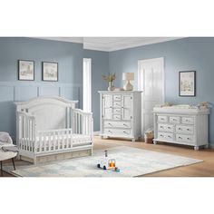 a baby's room with blue walls, white furniture and a rug on the floor