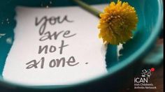 a yellow flower sitting in a blue bowl next to a note that says you are not alone