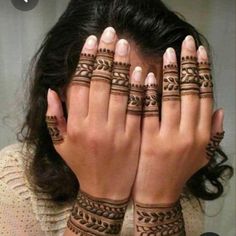 a woman holding her hands to her face with henna tattoos on it's arms