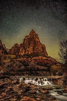 the stars are shining above some rocks and water in front of a rocky mountain range