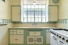 an old fashioned kitchen with green and white painted cabinets, stove top oven and sink