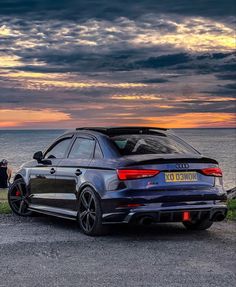 a blue car parked on the side of a road next to the ocean at sunset