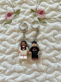 two lego keychains that have been placed on top of a white bed with pink flowers