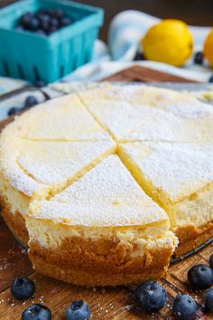 a cake that has been cut into slices on a cutting board with blueberries and lemons in the background