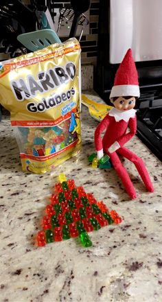 an elf is sitting on the counter next to some gummy bears and a bag of harro goldfingers