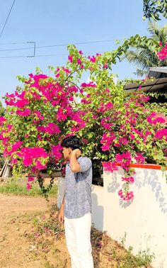 a man standing next to a bush with pink flowers