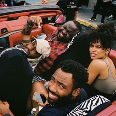 three people sitting in the back of a red car with one person holding a cell phone