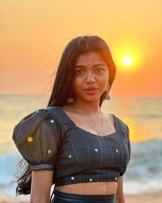 a woman standing on top of a beach next to the ocean at sun set with her hair blowing in the wind